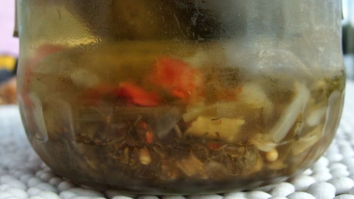 In einem Glas befindet sich Rest&ouml;l von eingelegten Paprika, umgeben von Gew&uuml;rzen und kleinen St&uuml;cken, die im &Ouml;l schwimmen.