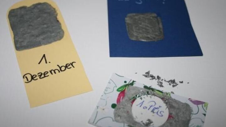 Drei Rubbellose mit Acrylfarbe zeigen verschiedene Designs und Zahlen: 1. Dezember, "Was gilt?" und "Advent".