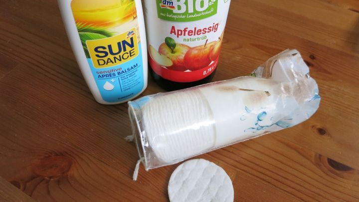 Eine Flasche Apfelessig, eine Flasche SUNDANCE Apres Balsam und ein Stapel Wattepads stehen auf einem Holztisch.