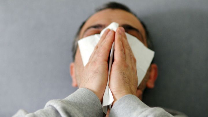 Ein Mann sitzt auf einem Sofa, h&auml;lt sich ein Taschentuch vor das Gesicht und scheint unter einer Erk&auml;ltung zu leiden.