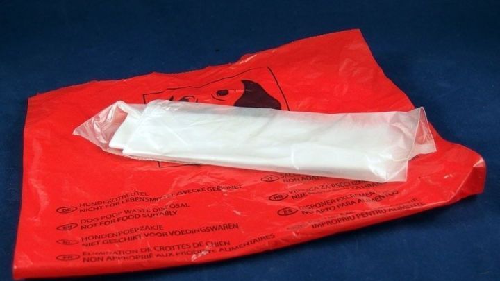 Ein roter Kotbeutel liegt neben einem wei&szlig;en, einzelnen Beutel auf einem blauen Hintergrund, bereit f&uuml;r die Nutzung.