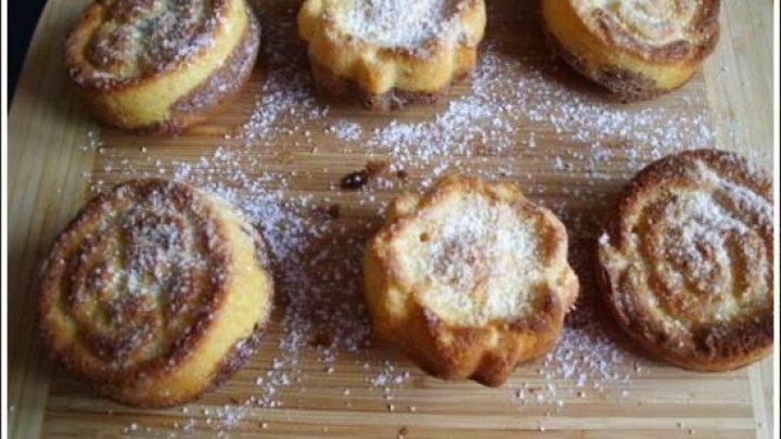Sechs Marmorkuchen-Muffins liegen auf einem Holzbrett, bestreut mit Puderzucker, frisch gebacken und appetitlich angerichtet.