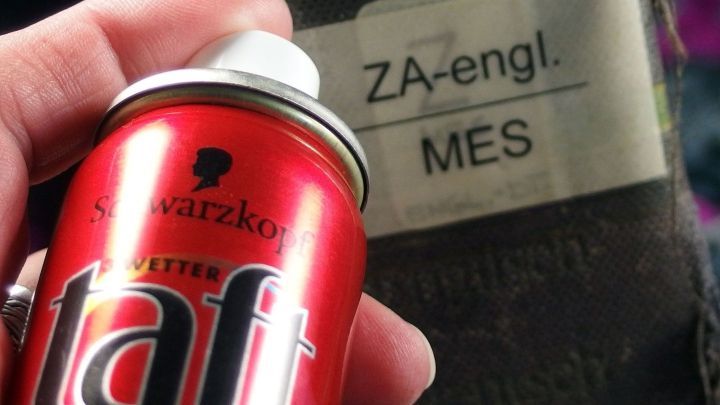 Eine rote Haarspraydose von Schwarzkopf Taft wird von einer Hand gehalten. Im Hintergrund ist ein Etikett mit "ZA-engl. MES".