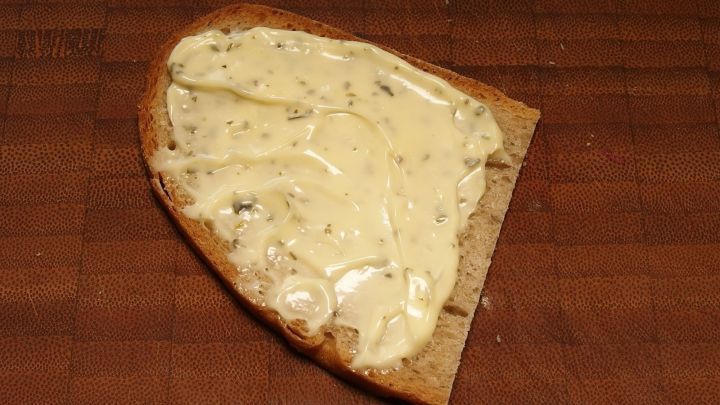 Ein St&uuml;ck Brot ist mit Remoulade bestrichen und liegt auf einer Holzoberfl&auml;che, umgeben von einer rustikalen Atmosph&auml;re.