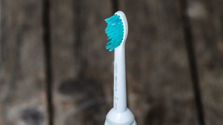 Eine elektrische Zahnb&uuml;rste steht auf einem rustikalen Holzuntergrund. Sie zeigt einen Aufsatz und zwei Tasten.