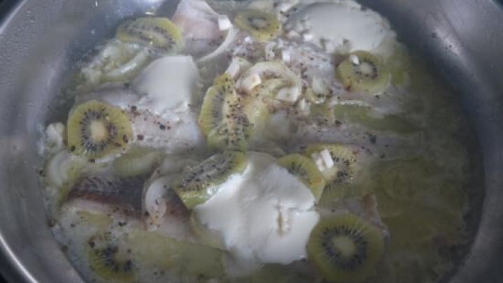 In einer Pfanne ist Seelachs in einer Br&uuml;he mit Zwiebeln und Gew&uuml;rzen am Kochen. Das Wasser sprudelt leicht.