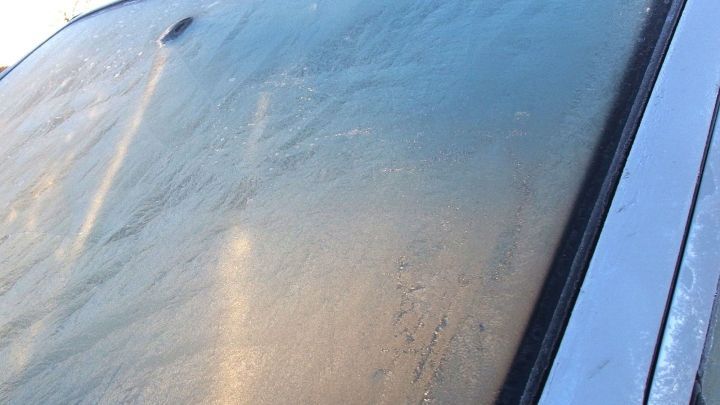 Eine gefrorene Windschutzscheibe zeigt Eisbildung, die im fr&uuml;hen Morgenlicht schimmert, bereit zum Auftauen.