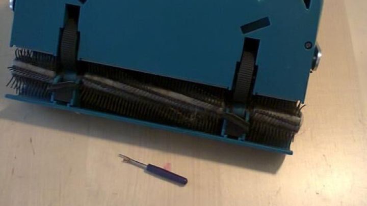 Ein manueller Teppichkehrer liegt auf einem Holztisch, w&auml;hrend ein kleiner Schraubendreher daneben platziert ist.