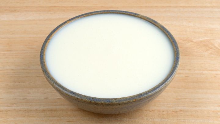 Eine Sch&uuml;ssel mit frischer Buttermilch steht auf einer Holzoberfl&auml;che und zeigt eine glatte, cremige Textur.