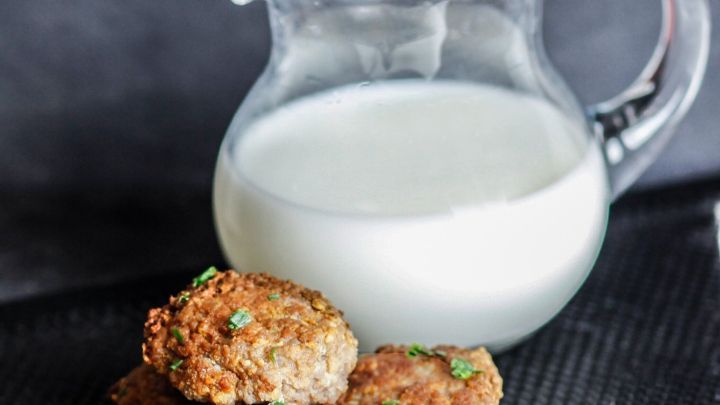 Saftige Frikadellen liegen neben einer Kanne mit frischer Milch auf einem dunklen Untergrund.