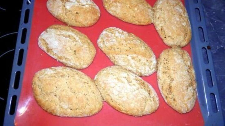 Auf einem Backblech liegen frisch gebackene Dinkelbr&ouml;tchen, goldbraun und knusprig, in einer modernen K&uuml;cheneinrichtung.