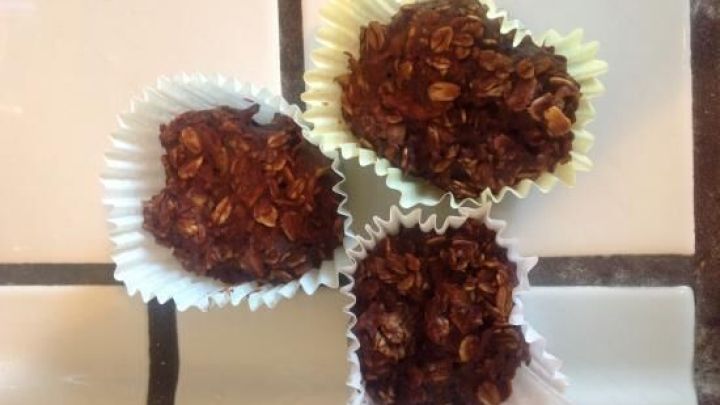 Drei Snack-Mini-Muffins in Papierf&ouml;rmchen liegen auf gefliester Fl&auml;che. Sie sind braun und bestehen aus Haferflocken.