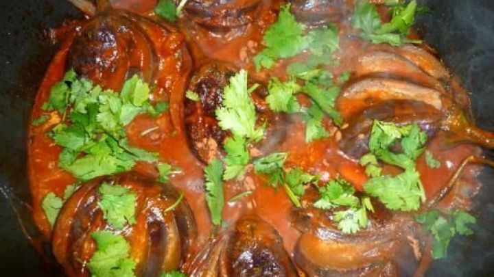 Geschmorte Baby Auberginen liegen in einer Tomatensauce, garniert mit frischem Koriander in einem Topf.