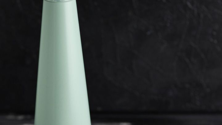 Ein gr&uuml;ner Spr&uuml;hbeh&auml;lter steht neben einem Haufen Natronpulver auf einer dunklen, glatten Oberfl&auml;che und wirkt frisch und sauber.