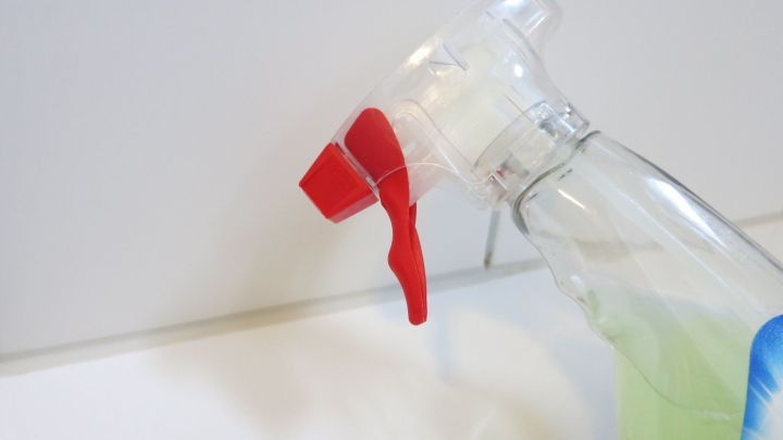 Eine Spr&uuml;hflasche mit rotem Spr&uuml;hkopf wird in Richtung einer gefliesten Wand gehalten, um Silikonfugen zu reinigen.