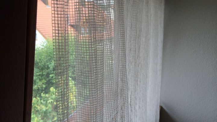 Transparente Gardinen h&auml;ngen vor einem Fenster und lassen Licht herein, w&auml;hrend die Aussicht auf einen Garten sichtbar bleibt.