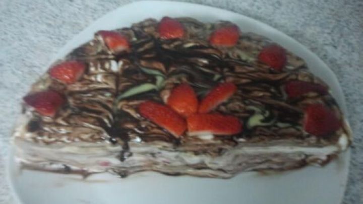 Eine Erdbeer-Bananen-Joghurt-Quark-Torte liegt auf einem wei&szlig;en Teller, dekoriert mit frischen Erdbeeren und Schokoladensauce.