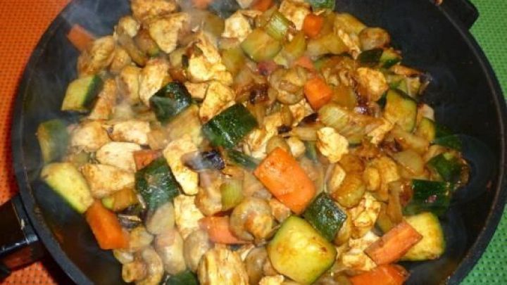 In einer Pfanne brutzeln bunte W&uuml;rfel von Gem&uuml;se und zarte H&uuml;hnerbrustfilets, umgeben von Dampf in einer hellen K&uuml;che.