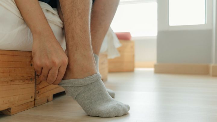 Eine Person zieht sich nasse Socken an, w&auml;hrend sie auf einem Bett sitzt, um sich vor Erk&auml;ltung zu sch&uuml;tzen.