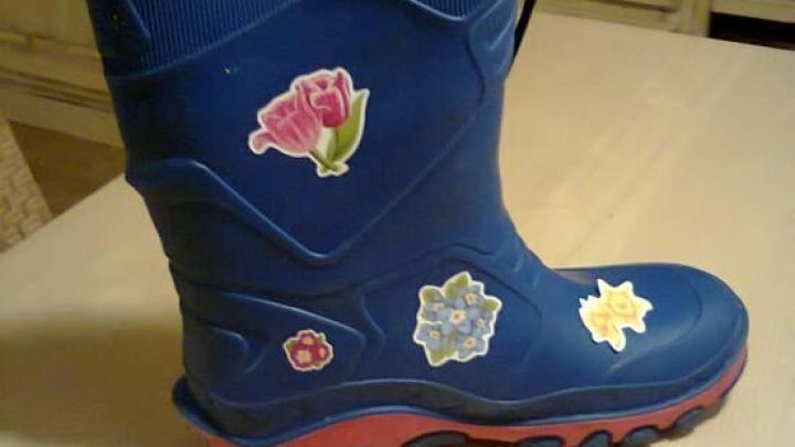 Ein blauer Gummistiefel f&uuml;r Kinder steht auf einem Tisch, dekoriert mit bunten Aufklebern von Blumen und Sternen.
