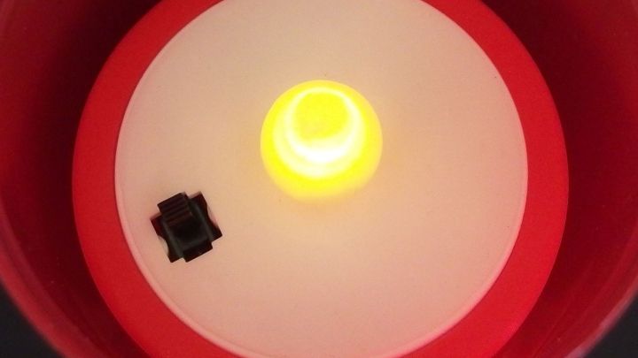 Eine LED-Kerze leuchtet in Gelb und erzeugt eine gem&uuml;tliche Atmosph&auml;re in einem runden, roten Kerzenhalter.