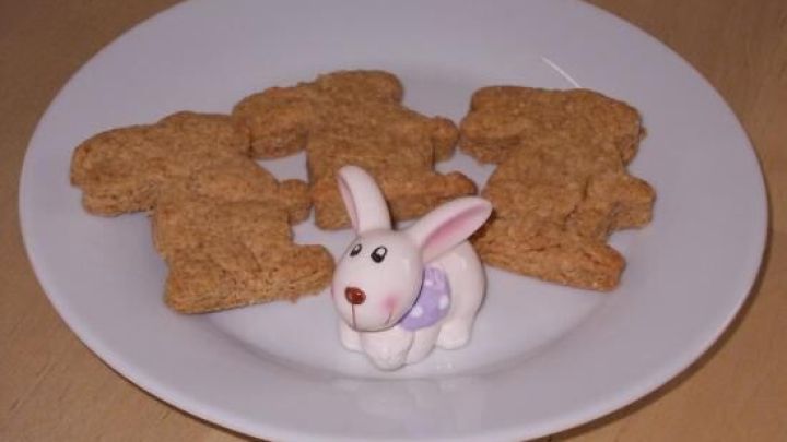 Kekse liegen auf einem wei&szlig;en Teller mit einem kleinen Keramikh&auml;schen in der Mitte, alles auf einem Holztisch.