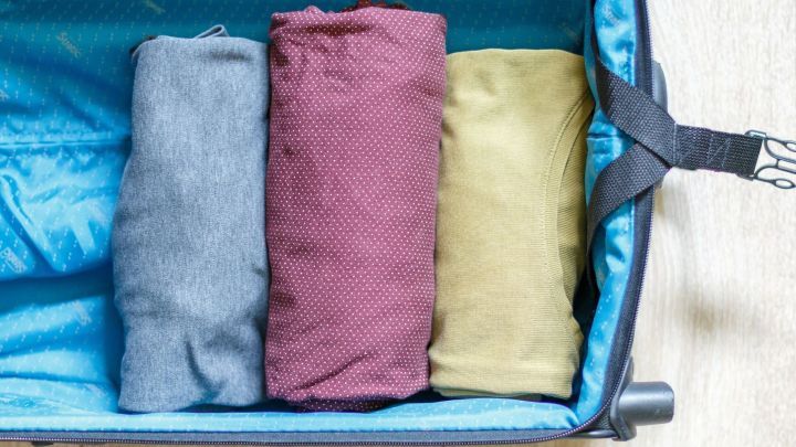 Drei ordentlich gerollte Kleidungsst&uuml;cke liegen in einem blauen Koffer, bereit zum cleveren Packen f&uuml;r die Reise.