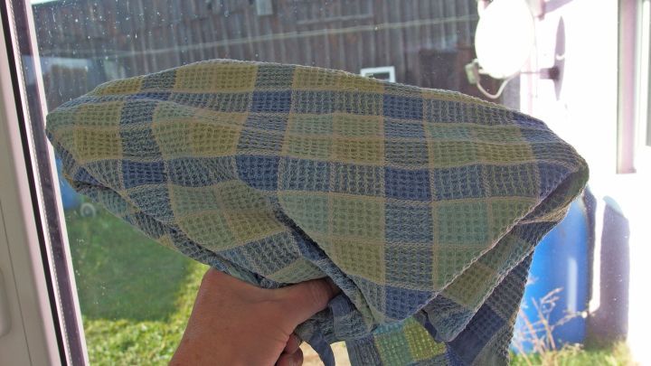 Ein Handtuch wird zum Fensterputzen genutzt, auf einer gr&uuml;nen Wiese stehend, vor einem dunklen Geb&auml;ude bei Tageslicht.