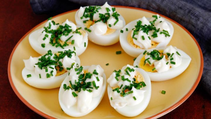 Sechs halbe Ostereier liegen auf einem Teller, dekoriert mit einer Schnittlauchcreme und frischem Schnittlauch.