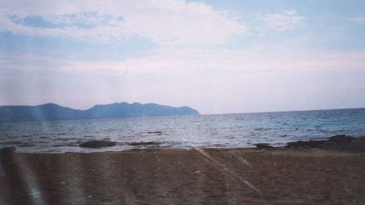 Ein sch&ouml;ner Strand erstreckt sich vor dem ruhigen Meer, das sanft gegen die Ufersteine pl&auml;tschert, unter einem blauen Himmel.