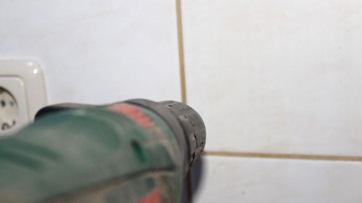 Eine bohrmaschine zielt pr&auml;zise auf eine Fliese, um punktgenau zu bohren, w&auml;hrend eine Steckdose im Hintergrund sichtbar ist.