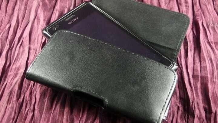 Eine elegante Schutzh&uuml;lle aus Leder f&uuml;r ein Handy liegt auf einem r&ouml;tlichen, strukturierten Stoff und sch&uuml;tzt das Ger&auml;t.