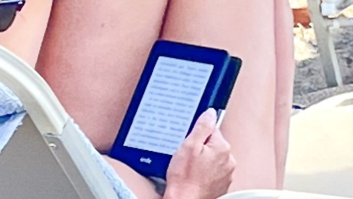 E-book-Reader wird am Strand liegend auf einer Sonnenliege gehalten, w&auml;hrend im Hintergrund das Meer zu sehen ist.