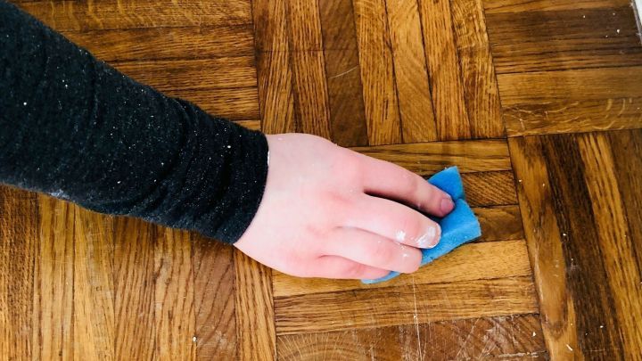 Ein Handtuch wischen einen Wachsfleck auf einem Parkettboden, um den Holzfu&szlig;boden zu reinigen und zu pflegen.