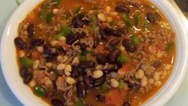 Eine wei&szlig;e Sch&uuml;ssel enth&auml;lt Partysuppe mit roten und wei&szlig;en Bohnen, Hackfleisch und Paprikast&uuml;cken, auf einem K&uuml;chentisch.