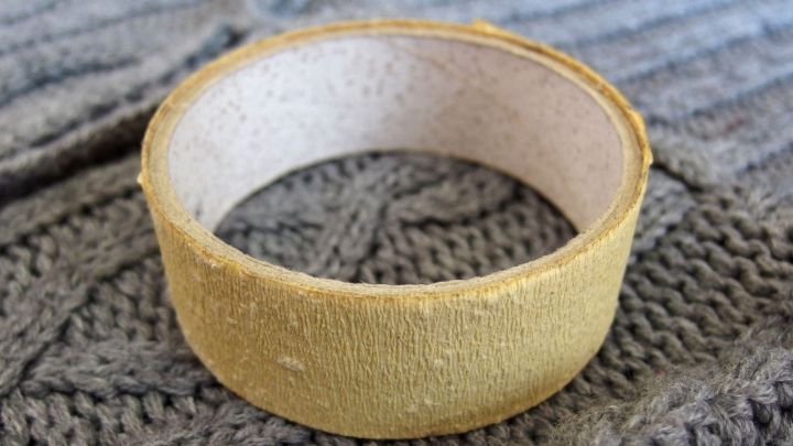 Ein gelber Fusselroller liegt auf einem grauen, gestrickten Pullover und dient zum Entfernen von Pferdehaaren.