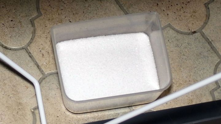 Ein transparenter Beh&auml;lter mit wei&szlig;em Pulver steht auf einem Bodenfliesen, wahrscheinlich zum Verhindern von beschlagenen Scheiben.