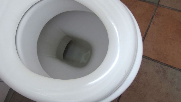 Eine matte Klobrille zeigt ihren inneren Bereich. Sie befindet sich in einem Badezimmer mit Fliesenboden.