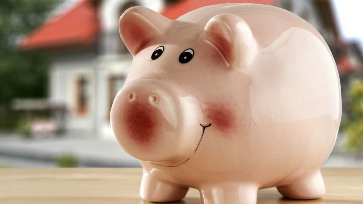 Eine rosa Sparschwein steht auf einem Tisch und ermutigt zum Geldsparen in einer gem&uuml;tlichen K&uuml;chenszene im Hintergrund.