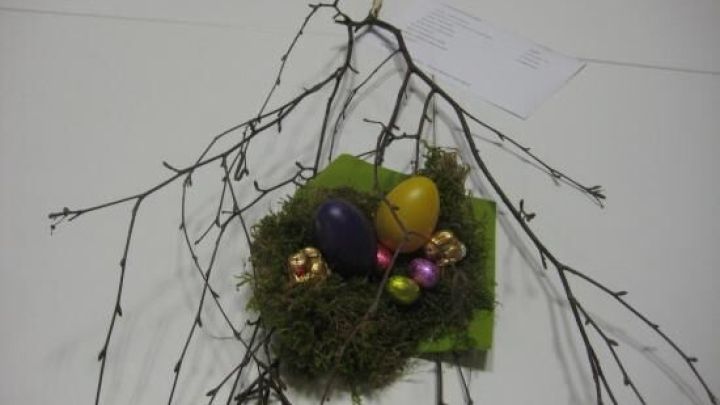 Ein dekorativer Ast mit bunten Ostereiern und Schokolade auf Moos, platziert auf einem wei&szlig;en Tisch f&uuml;r Osterdeko.