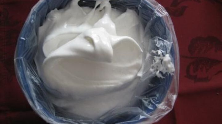 Ein Fr&uuml;hst&uuml;cksbeutel mit Spritzt&uuml;lle ist gef&uuml;llt mit luftiger Creme und auf einem roten Untergrund platziert.