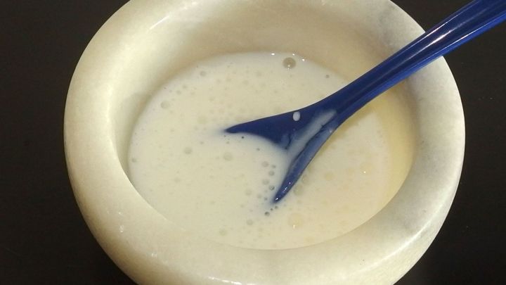 Eine cremige Gesichtsmaske aus Quark wird mit einem blauen L&ouml;ffel in einer wei&szlig;en Sch&uuml;ssel anger&uuml;hrt, vorbereitet f&uuml;r die Anwendung.