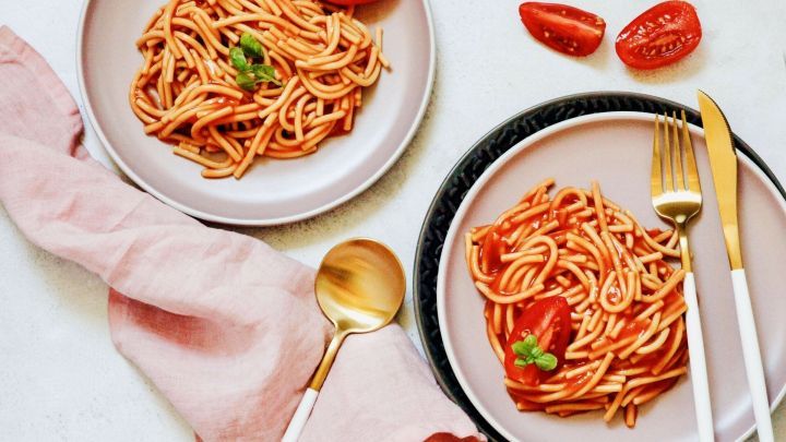 Zwei Teller mit Spaghetti in Tomatensauce stehen auf einem Tisch, umgeben von frischen Tomaten und Besteck.