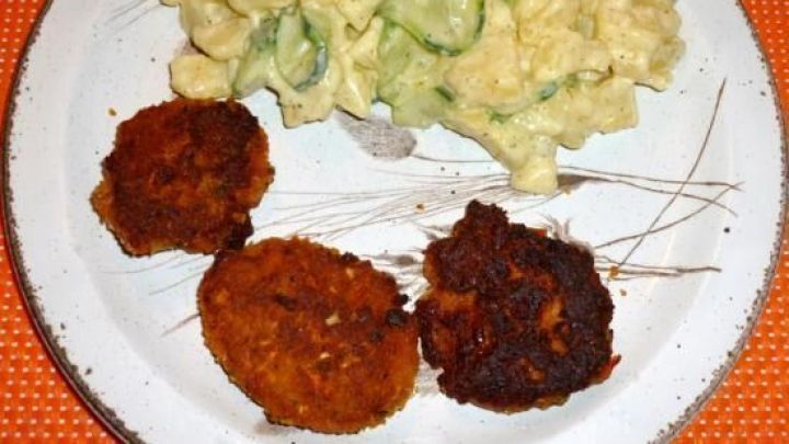 Drei Gem&uuml;seburger auf einem Teller, w&auml;hrend daneben ein cremiger Nudelsalat liegt, alles auf einem orangefarbenen Untergrund.