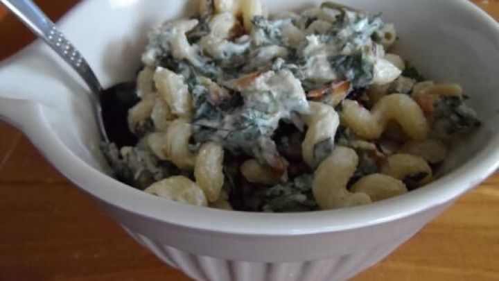 Ein mit L&ouml;wenzahn und Nudeln gef&uuml;llter Sch&uuml;ssel, gemischt mit einer cremigen Sauce, steht auf einem Holztisch.