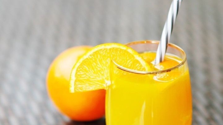 Ein erfrischender Sommer-Cocktail in einem klaren Glas steht mit einem gestreiften Strohhalm auf einer Holzoberfl&auml;che neben einer Orange.