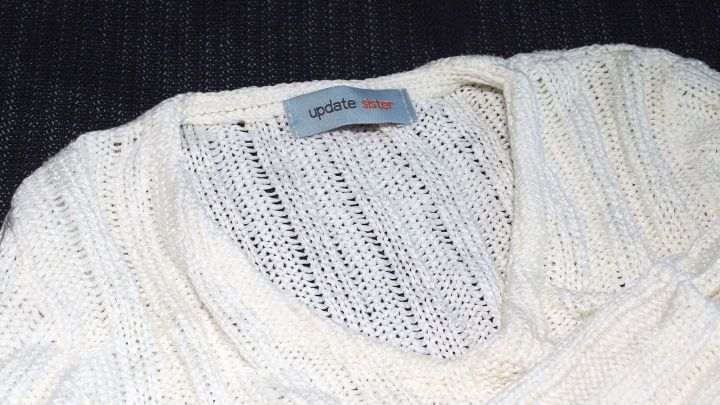 Ein wei&szlig;er Pullover mit einem weiten Ausschnitt liegt auf einem dunklen Hintergrund. Die Struktur ist grob und gestrickt.