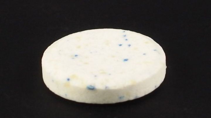 Eine runde, wei&szlig;e Reinigungstablette liegt auf schwarzem Untergrund, bereit, um eine Kaffeemaschine mit Kukident zu entkalken.