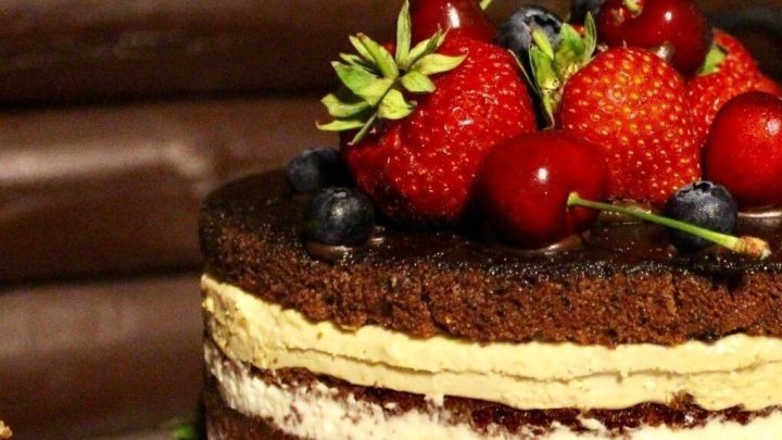 Ein &uuml;ppiger Schokoladenkuchen mit fruchtigem Tortenbelag, dekoriert mit Erdbeeren und Heidelbeeren, steht auf einem Tisch.