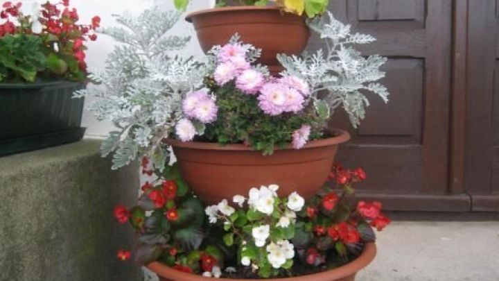 Ein Blumenturm aus gestapelten Blumenschalen mit bunten Blumen steht vor einer Holzwand und einer Zementstufe.